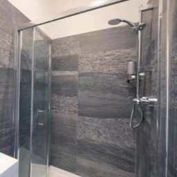 Neutral-toned bathroom with a oval mirror, modern sink, and shower area visible.